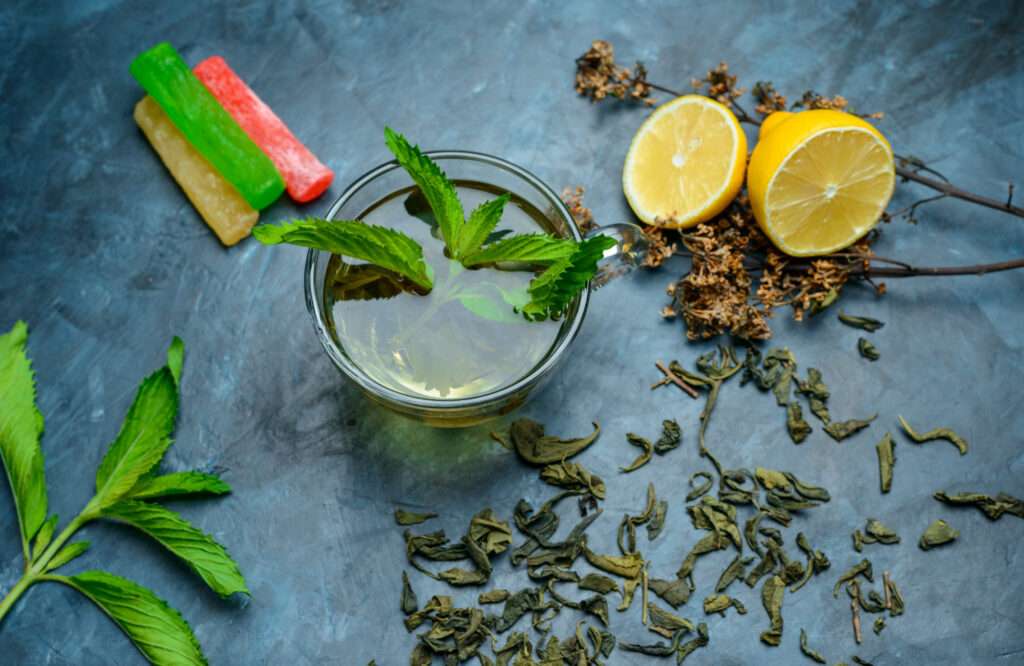 tea cup with mint dried herbs lemon sweeties flat lay dark blue surface